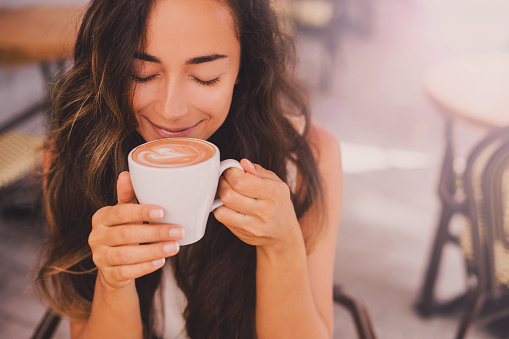 Young beautiful happy woman with long curly hair enjoying cappuccino at the beach java cafe